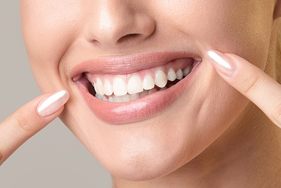 Woman with bright smile showing teeth, holding her face with both hands, seemingly happy or surprised.