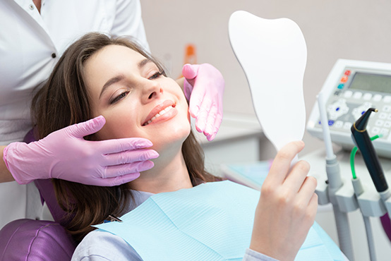 A woman sitting in a dental chair with a dentist s mirror in front of her, receiving dental care.