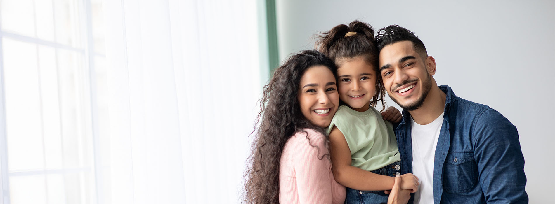 A family of four poses together with smiles, featuring two adults and two children, one holding a baby.