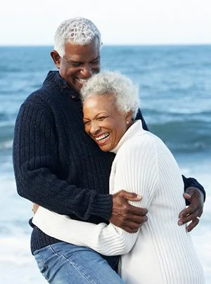 Senior couple with implant dentures hugging on beach in Trinity FL